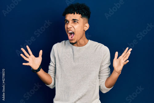 Young african american man wearing casual clothes crazy and mad shouting and yelling with aggressive expression and arms raised. frustration concept.