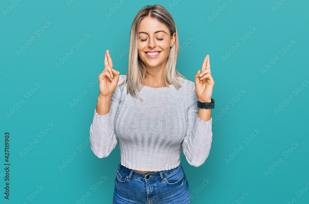 Beautiful blonde woman wearing casual clothes gesturing finger crossed smiling with hope and eyes closed. luck and superstitious concept. Beautiful blonde woman wearing casual clothes gesturing finger crossed smiling with hope and eyes closed. luck and superstitious concept.