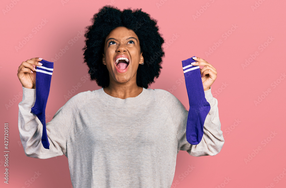 Young african american woman holding socks angry and mad screaming frustrated and furious, shouting with anger looking up. Young african american woman holding socks angry and mad screaming frustrated and furious, shouting with anger looking up.