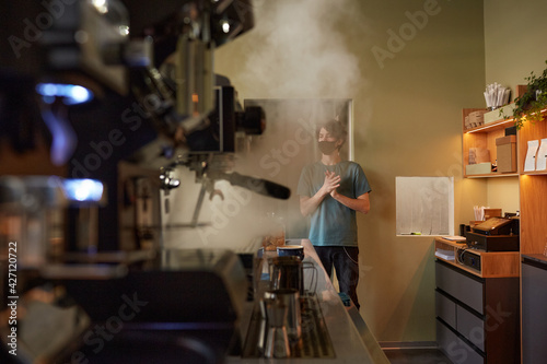 Close up of steaming coffee machine at bar counter in cafe or coffee shop with barista wearing mask in background  copy space