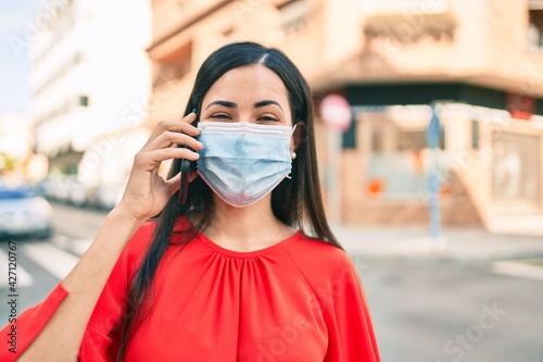 Young latin girl wearing medical mask talking on the smartphone at the city.