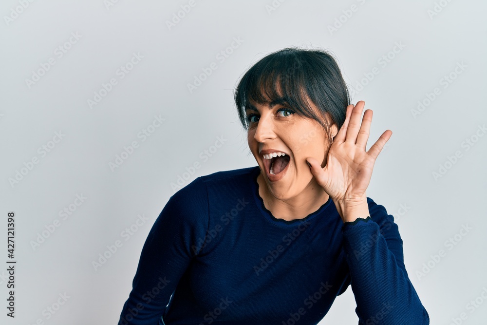 Young hispanic woman wearing casual clothes smiling with hand over ear listening and hearing to rumor or gossip. deafness concept. Young hispanic woman wearing casual clothes smiling with hand over ear listening and hearing to rumor or gossip. deafness concept.