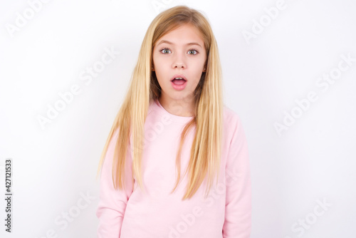 beautiful caucasian little girl wearing pink hoodie over white background having stunned and shocked look  with mouth open and jaw dropped exclaiming  Wow  I can t believe this. Surprise and shock