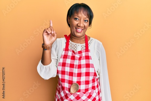 Middle age african american woman wearing baker uniform smiling with an idea or question pointing finger up with happy face, number one