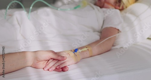 mother holding a hand of acutely sick kid with intravenous fluid therapy and oxygen mask for lung ventilation