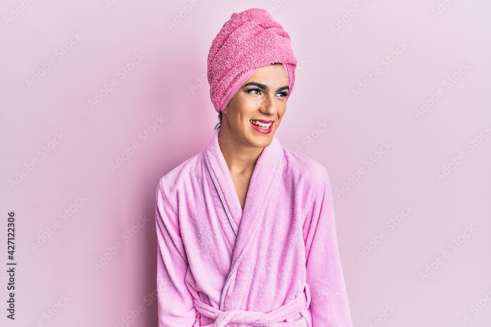Young man wearing woman make up wearing shower towel on head and bathrobe smiling looking to the side and staring away thinking. Young man wearing woman make up wearing shower towel on head and bathrobe smiling looking to the side and staring away thinking.
