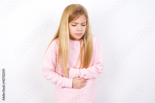 beautiful caucasian little girl wearing pink hoodie over white background suffering from strong stomachache.