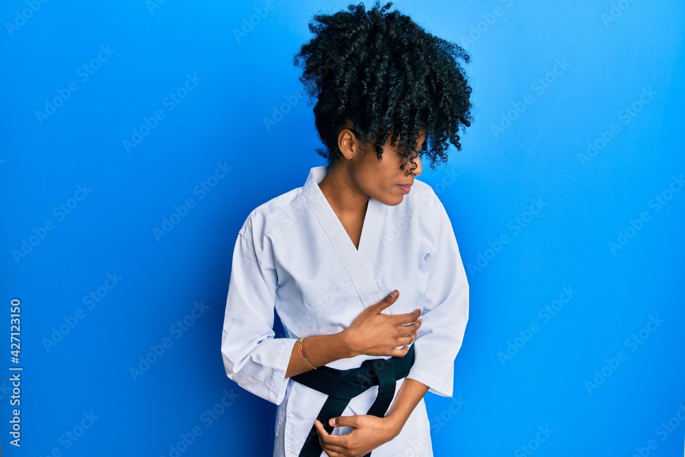 African american woman with afro hair wearing karate kimono and black belt with hand on stomach because indigestion, painful illness feeling unwell. ache concept. African american woman with afro hair wearing karate kimono and black belt with hand on stomach because indigestion, painful illness feeling unwell. ache concept.