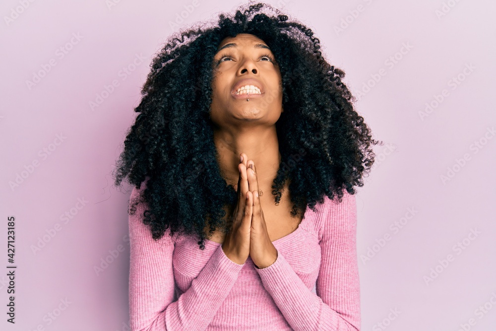 African american woman with afro hair wearing casual pink shirt begging and praying with hands together with hope expression on face very emotional and worried. begging.