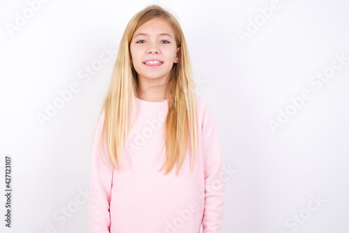 beautiful caucasian little girl wearing pink hoodie over white background with happy and funny face smiling and showing tongue.