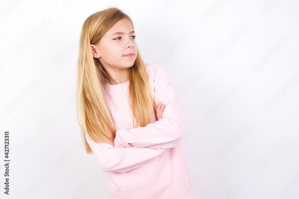 Image of upset beautiful caucasian little girl wearing pink hoodie over white background with arms crossed. Looking with disappointed expression aside after listening to bad news. Image of upset beautiful caucasian little girl wearing pink hoodie over white background with arms crossed. Looking with disappointed expression aside after listening to bad news.