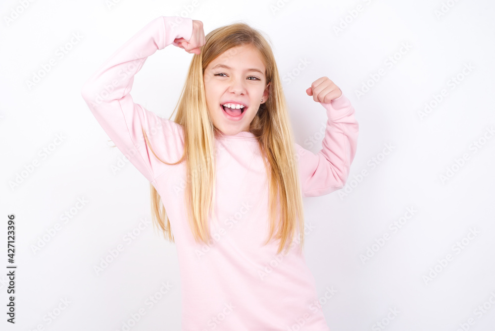 Fototapeta premium Yes I am winner. Portrait of charming delighted and excited beautiful caucasian little girl wearing pink hoodie raising up fist in triumph and victory smiling achieving success grinning from delight.
