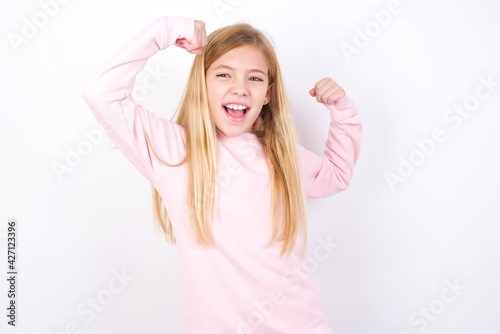 Yes I am winner. Portrait of charming delighted and excited beautiful caucasian little girl wearing pink hoodie  raising up fist in triumph and victory smiling achieving success grinning from delight.