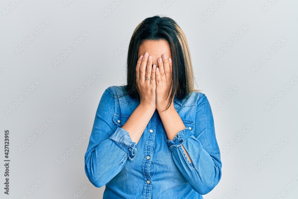 Young hispanic woman wearing casual denim jacket with sad expression covering face with hands while crying. depression concept. Young hispanic woman wearing casual denim jacket with sad expression covering face with hands while crying. depression concept.