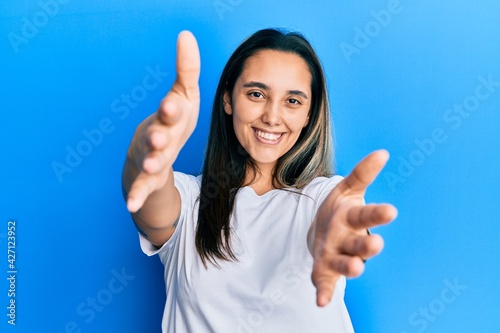 Young hispanic woman wearing casual white t shirt looking at the camera smiling with open arms for hug. cheerful expression embracing happiness. © Krakenimages.com