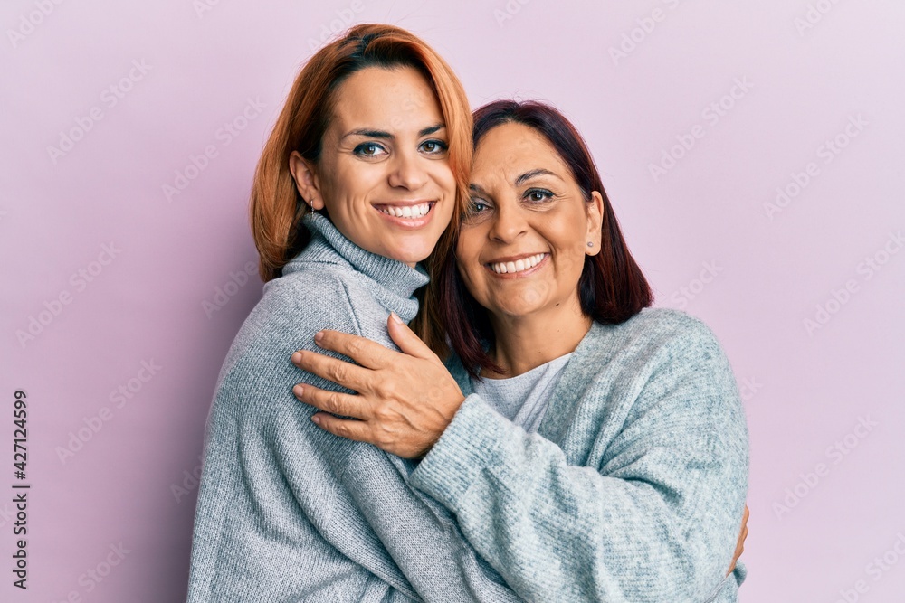 Hispanic mother and daughter smiling happy and hugging standing over isolated pink background. Hispanic mother and daughter smiling happy and hugging standing over isolated pink background.