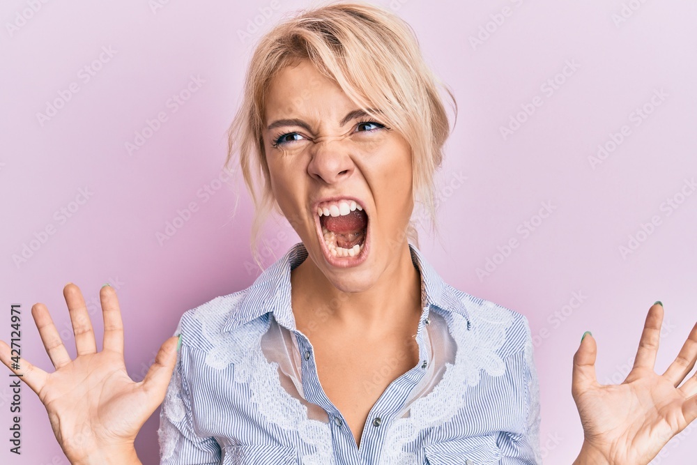 Young blonde girl wearing casual clothes crazy and mad shouting and yelling with aggressive expression and arms raised. frustration concept. Young blonde girl wearing casual clothes crazy and mad shouting and yelling with aggressive expression and arms raised. frustration concept.