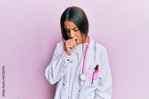 Beautiful hispanic woman wearing doctor uniform and stethoscope feeling unwell and coughing as symptom for cold or bronchitis. health care concept.