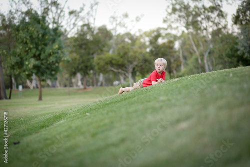 Little boy lying on beautiful grassy green hill and rolling down. Nature fun with children.