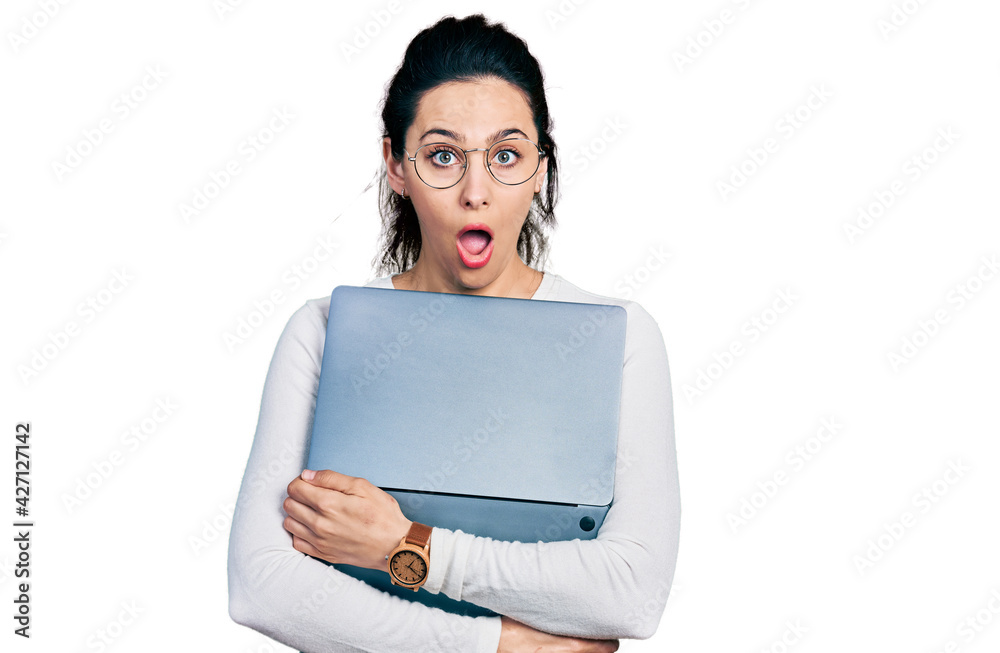 Young hispanic woman working using computer laptop afraid and shocked with surprise and amazed expression, fear and excited face. Young hispanic woman working using computer laptop afraid and shocked with surprise and amazed expression, fear and excited face.