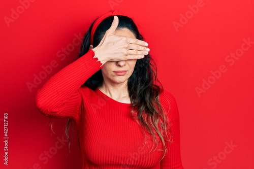 Young hispanic woman wearing casual clothes covering eyes with hand, looking serious and sad. sightless, hiding and rejection concept