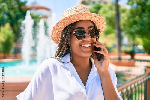 Young african american woman with braids smiling happy spaking on the phone outdoors on a sunny day of summer