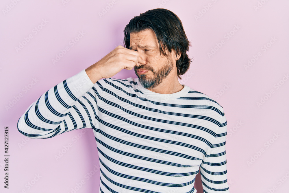 Middle age caucasian man wearing casual clothes smelling something stinky and disgusting, intolerable smell, holding breath with fingers on nose. bad smell Middle age caucasian man wearing casual clothes smelling something stinky and disgusting, intolerable smell, holding breath with fingers on nose. bad smell