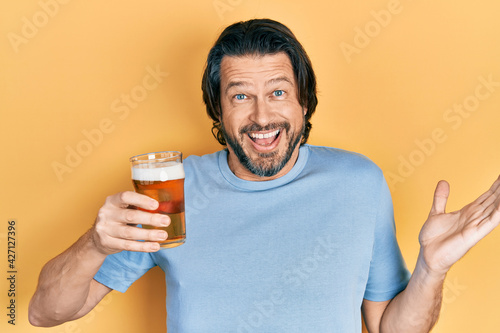 Middle age caucasian man drinking a pint of beer celebrating achievement with happy smile and winner expression with raised hand