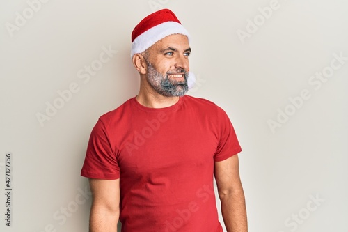 Middle age handsome man wearing christmas hat and summer t-shirt looking to side, relax profile pose with natural face and confident smile.
