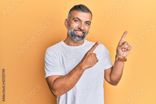 Middle age handsome man wearing casual white tshirt smiling and looking at the camera pointing with two hands and fingers to the side.