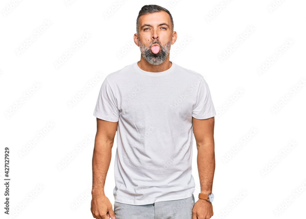 Middle age handsome man wearing casual white tshirt sticking tongue out happy with funny expression. emotion concept.