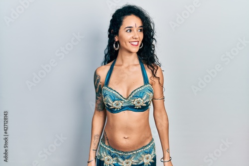 Young woman wearing bindi and traditional belly dance clothes looking away to side with smile on face, natural expression. laughing confident.