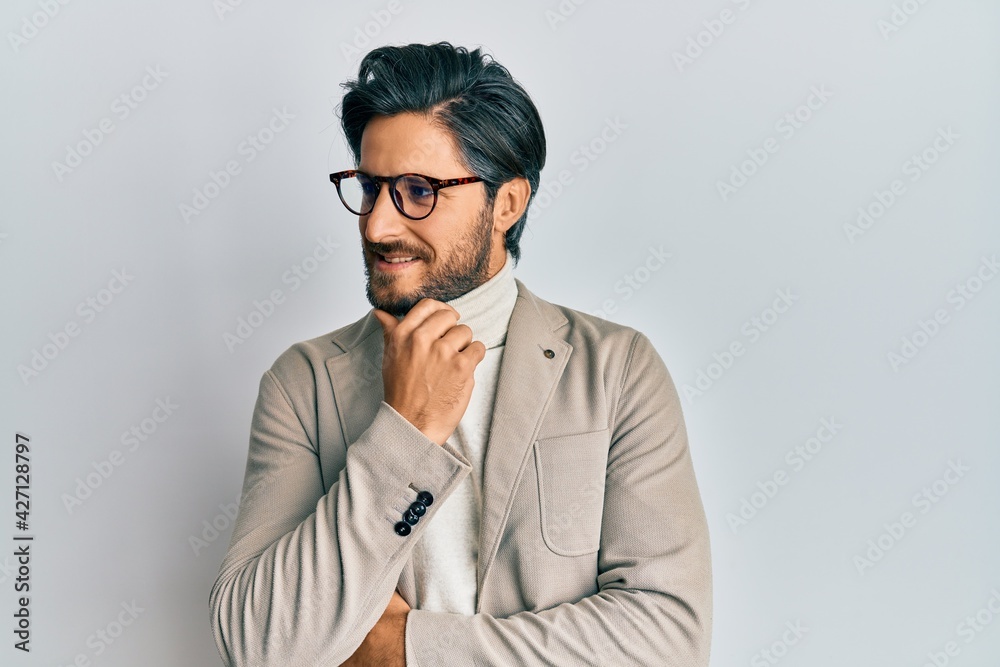 Young hispanic man wearing business jacket and glasses with hand on chin thinking about question, pensive expression. smiling with thoughtful face. doubt concept. Young hispanic man wearing business jacket and glasses with hand on chin thinking about question, pensive expression. smiling with thoughtful face. doubt concept.