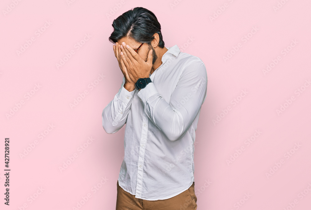 Young hispanic man wearing business shirt and glasses with sad expression covering face with hands while crying. depression concept. Young hispanic man wearing business shirt and glasses with sad expression covering face with hands while crying. depression concept.