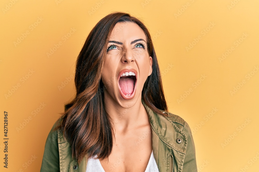 Young brunette woman wearing casual clothes over yellow background angry and mad screaming frustrated and furious, shouting with anger looking up. Young brunette woman wearing casual clothes over yellow background angry and mad screaming frustrated and furious, shouting with anger looking up.