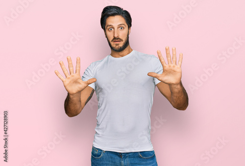 Cuadro en lienzo Young hispanic man wearing casual white t shirt afraid and terrified with fear expression stop gesture with hands, shouting in shock