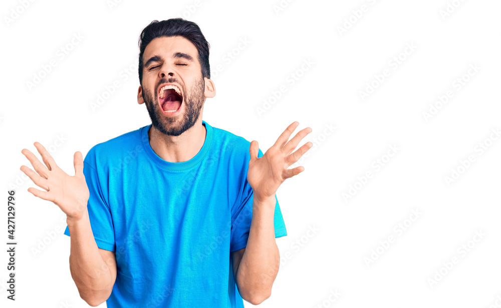 Fototapeta premium Young handsome man with beard wearing casual t-shirt celebrating mad and crazy for success with arms raised and closed eyes screaming excited. winner concept