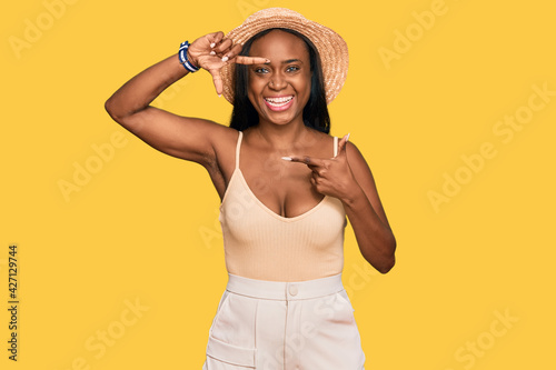 Young black woman wearing summer hat smiling making frame with hands and fingers with happy face. creativity and photography concept.