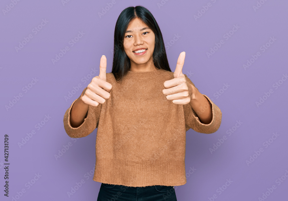 Beautiful young asian woman wearing casual winter sweater approving doing positive gesture with hand, thumbs up smiling and happy for success. winner gesture. Beautiful young asian woman wearing casual winter sweater approving doing positive gesture with hand, thumbs up smiling and happy for success. winner gesture.