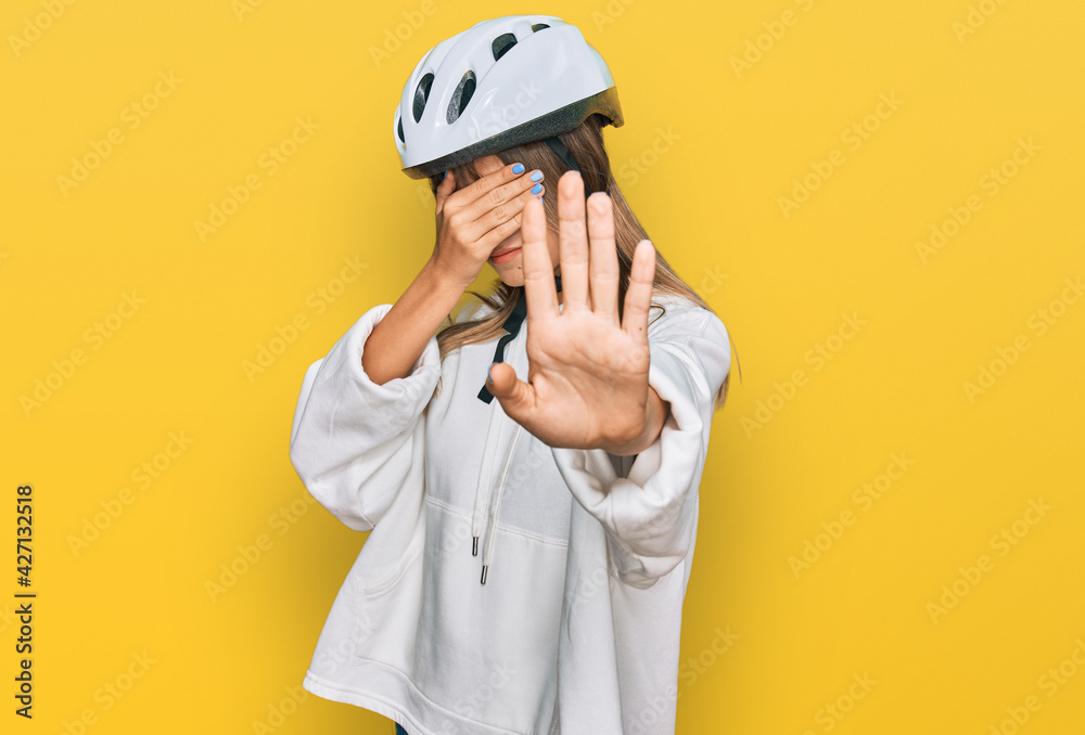 Teenager caucasian girl wearing bike helmet covering eyes with hands and doing stop gesture with sad and fear expression. embarrassed and negative concept. Teenager caucasian girl wearing bike helmet covering eyes with hands and doing stop gesture with sad and fear expression. embarrassed and negative concept.