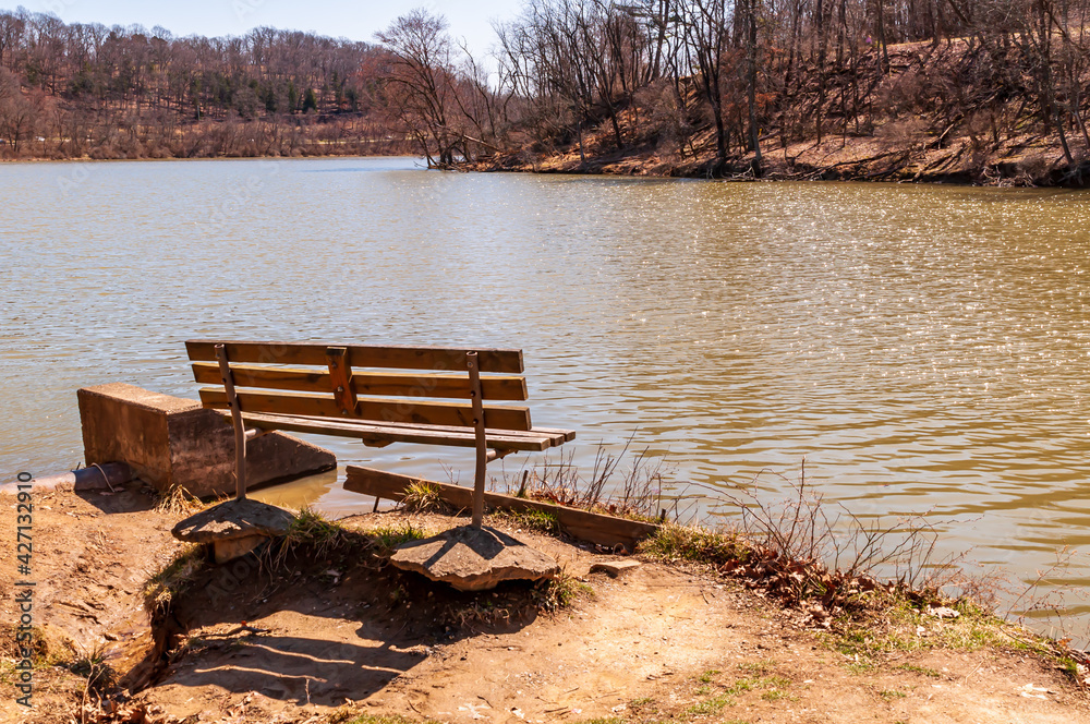 A park bench next to the North Park lake on a sunny spring day in Hampton Township, Pennsylvania, USA