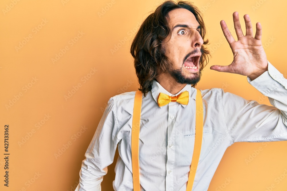 Young hispanic man wearing hipster elegant look shouting and screaming loud to side with hand on mouth. communication concept. Young hispanic man wearing hipster elegant look shouting and screaming loud to side with hand on mouth. communication concept.