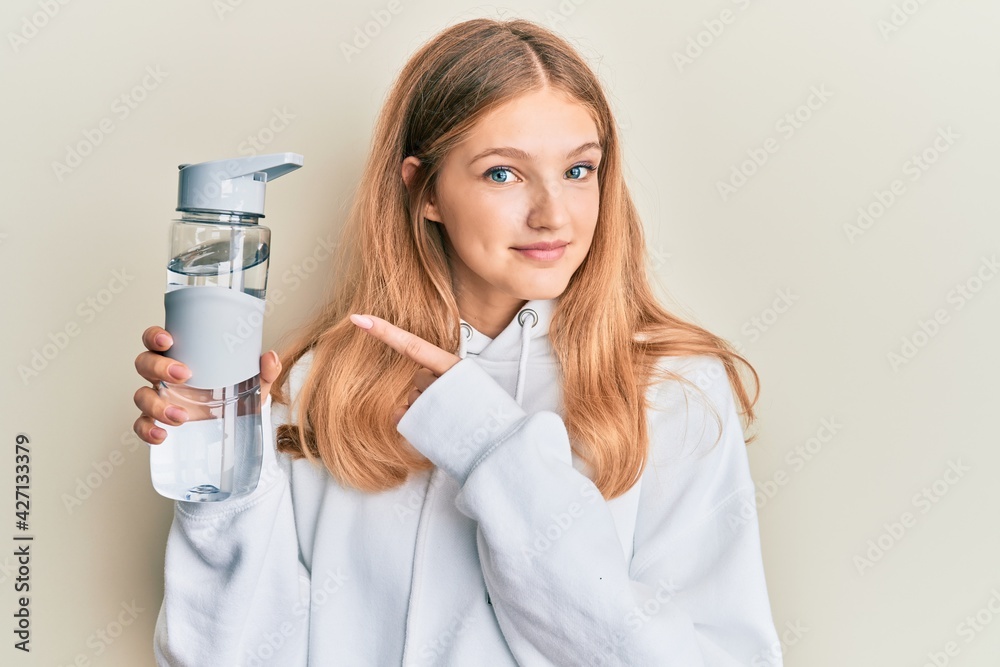 Beautiful young caucasian girl wearing sportswear drinking bottle of water smiling happy pointing with hand and finger Beautiful young caucasian girl wearing sportswear drinking bottle of water smiling happy pointing with hand and finger