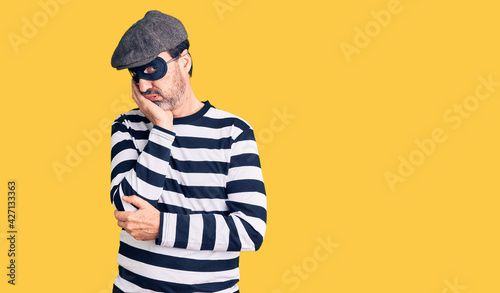 Middle age handsome man wearing burglar mask thinking looking tired and bored with depression problems with crossed arms.