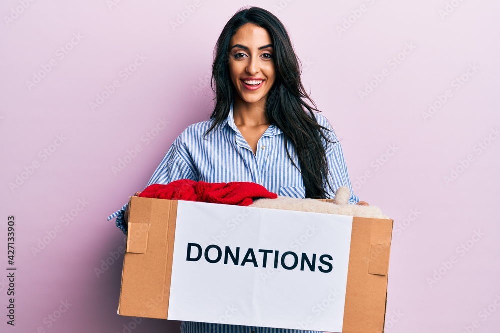 Beautiful hispanic woman volunteer holding donations box smiling and laughing hard out loud because funny crazy joke. Beautiful hispanic woman volunteer holding donations box smiling and laughing hard out loud because funny crazy joke.