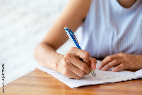 Close up hand of business women use pen writing document paper. Female hand close up writing with a blue pen on a white sheet. Woman writes information on a piece of paper.