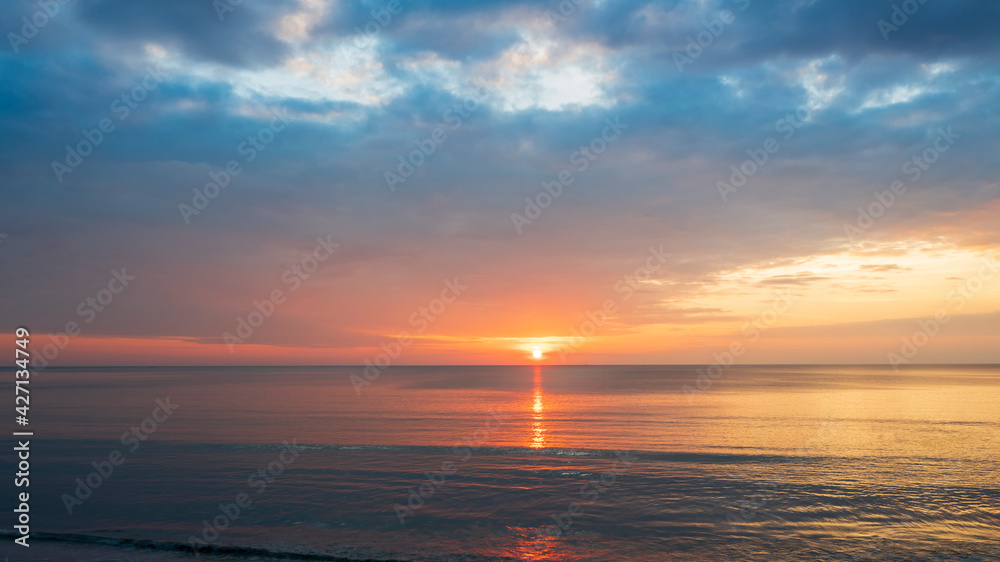 Beautiful sunset over the clam sea with cloud sky background. Sunset over tropical beach. Nature summer  concept. Peak sunset over sea with yellow light reflect on sea water. 