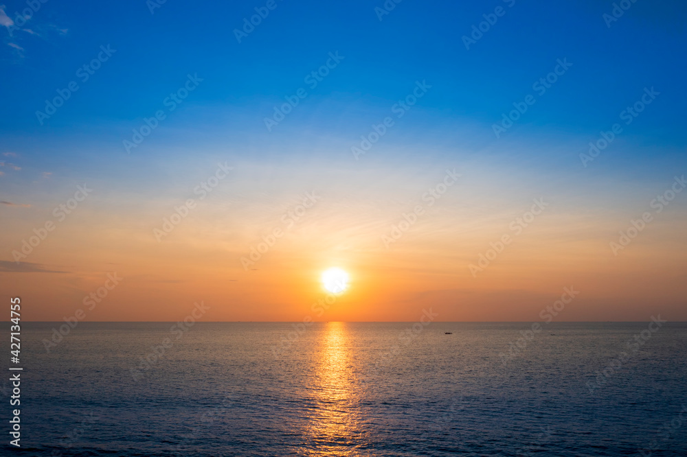 Beautiful sunset over the clam sea with cloud sky background. Sunset over tropical beach. Nature summer  concept. Peak sunset over sea with yellow light reflect on sea water. 