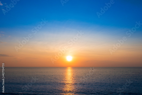 Beautiful sunset over the clam sea with cloud sky background. Sunset over tropical beach. Nature summer concept. Peak sunset over sea with yellow light reflect on sea water. 