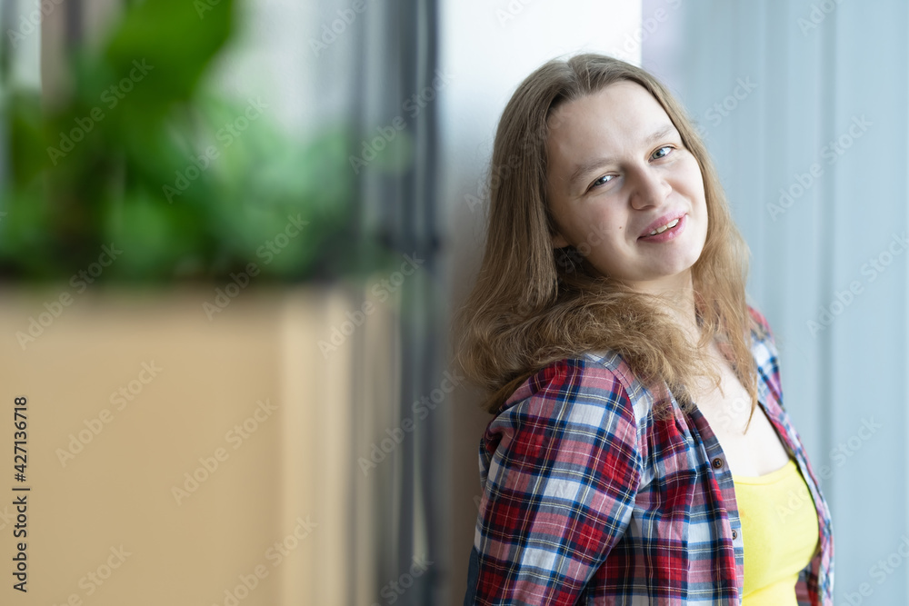 girl in a plaid shirt stands near a window in a shopping center. pensive view. on the background of a green flower bed girl in a plaid shirt stands near a window in a shopping center. pensive view. on the background of a green flower bed